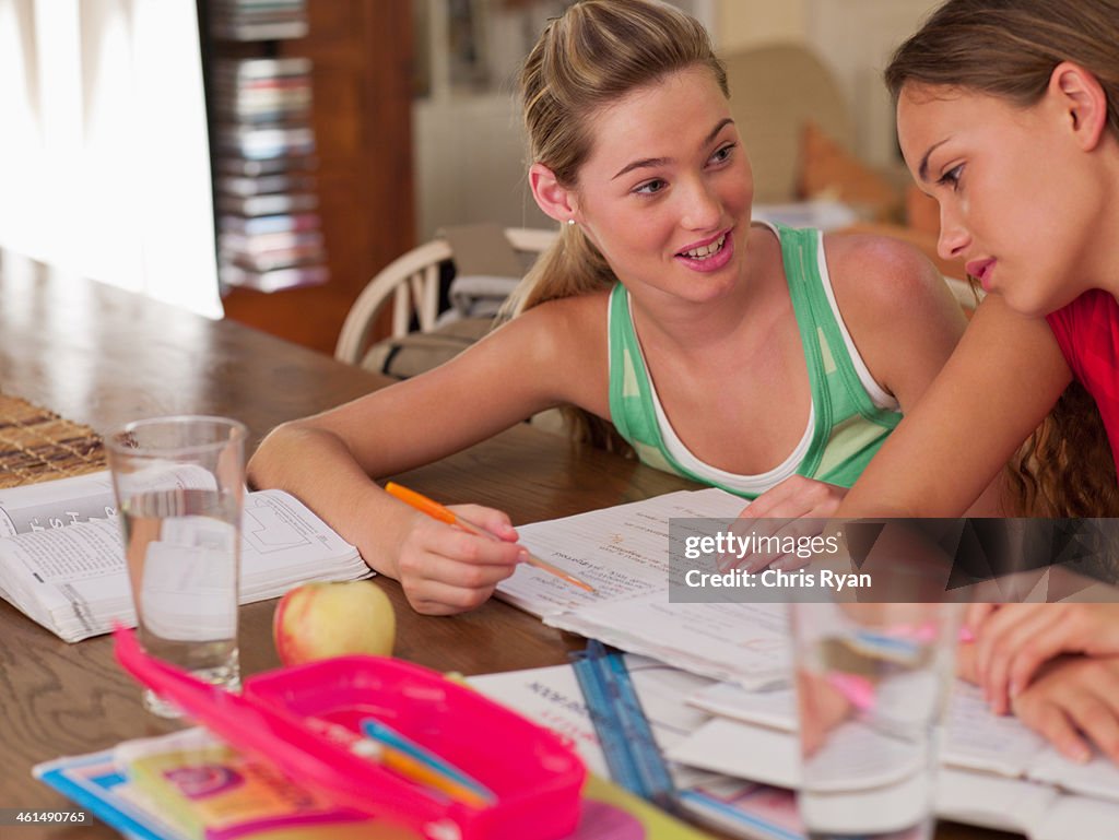 Two teenage girls sitting at table studying and smiling