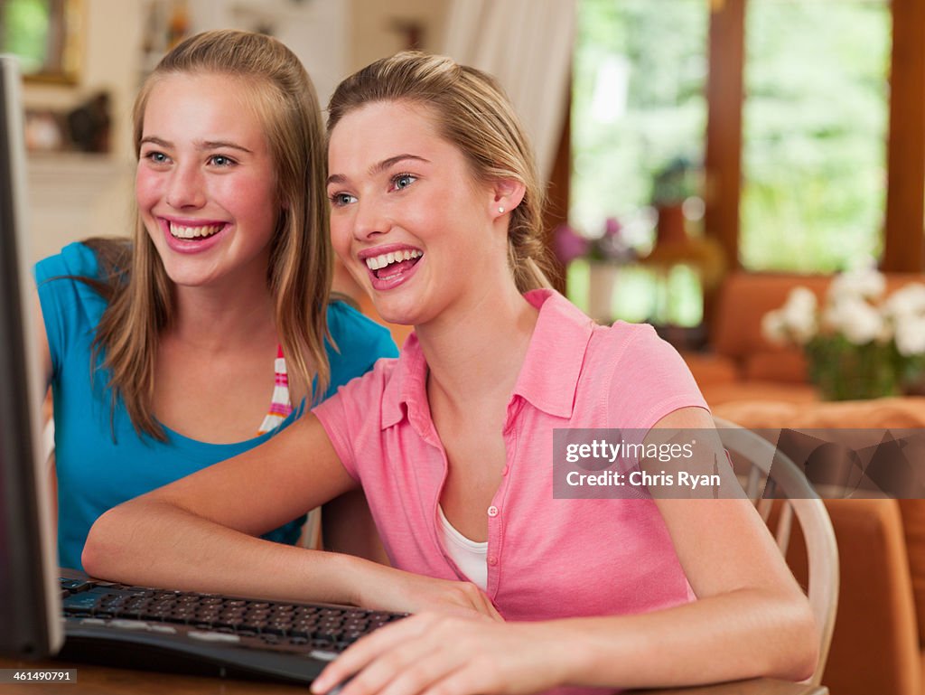 Two teenage girls sitting at table looking at computer monitor