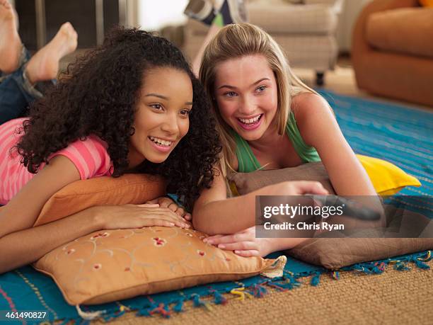 two teenage girls lying down watching television with remote control smiling - girl looking down stock pictures, royalty-free photos & images