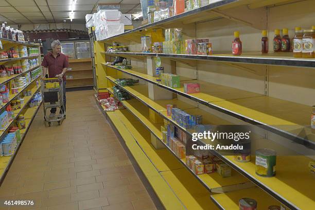 Shopper walks past nearly empty shelves at a supermarket due to a long term shortage in Caracas, Venezuela on January 13, 2015. Sliding oil prices...