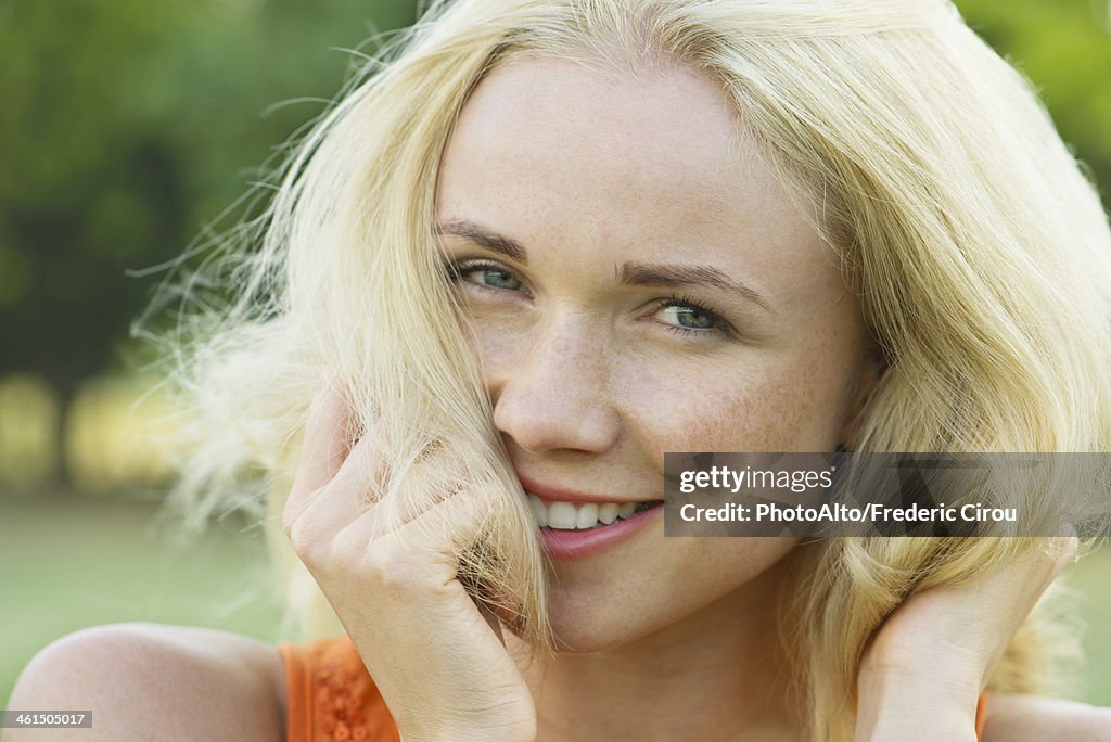 Young woman with hands in hair, smiling, portrait