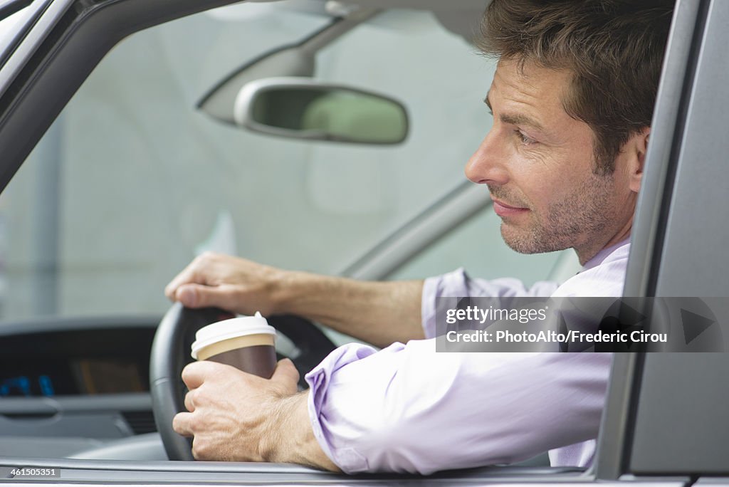 Man driving car with cup of coffee in one hand