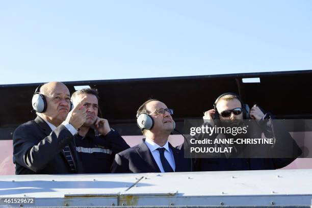 French President Francois Hollande looks at an military aircraft flying, flanked by French Defence Minister Jean-Yves Le Drian and with French...