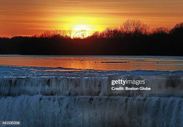 Birds are perched on patches of ice in the Merrimack River near the Great Stone Dam as the sun sets on a cold day.