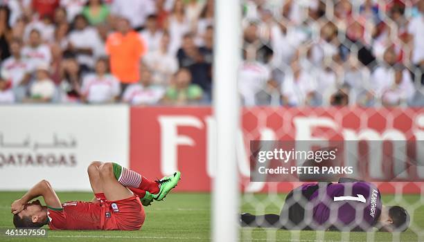 Vouria Ghafouri and goalkeeper Alireza Haghighi of Iran lie on the ground after clashing during their game against Qatar in their Group C football...