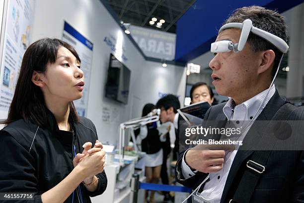 Visitor, right, tries out a Brother Industries Ltd.'s AiRScouter head-mounted display as he speaks to an attendant at the Wearable Expo in Tokyo,...