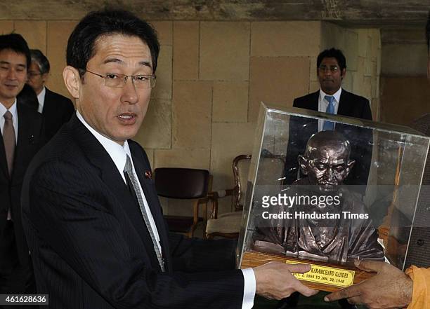 Japanese Foreign Minister Fumio Kishida poses with a bust of Mahatma Gandhi presented to him during his visit at Rajghat on January 16, 2015 in New...