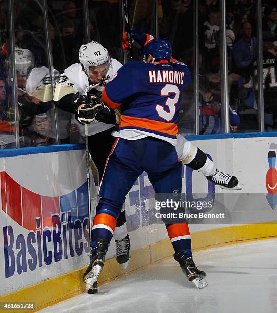 Travis Hamonic of the New York Islanders hits Sidney Crosby of the Pittsburgh Penguins into the boards during the third period at the Nassau Veterans...