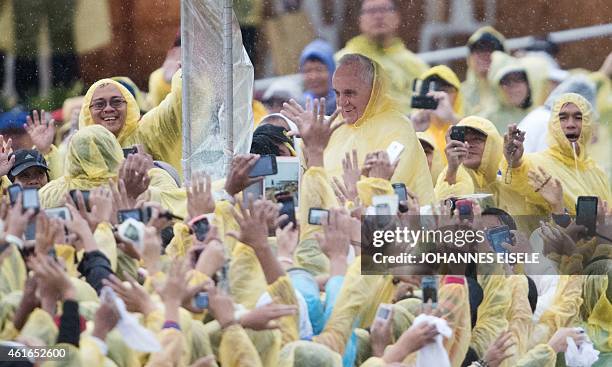 Pope Francis wears a plastic poncho as he waves to well wishers after a mass in Tacloban on January 17, 2015. Pope Francis will spend an emotional...
