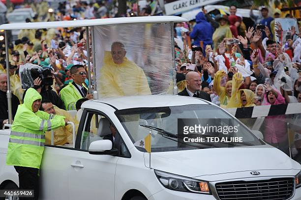 Pope Francis , wearing a yellow raincoat, smiles at the crowd as he travels from Tacloban airport to the town of Palo after celebrating mass on...