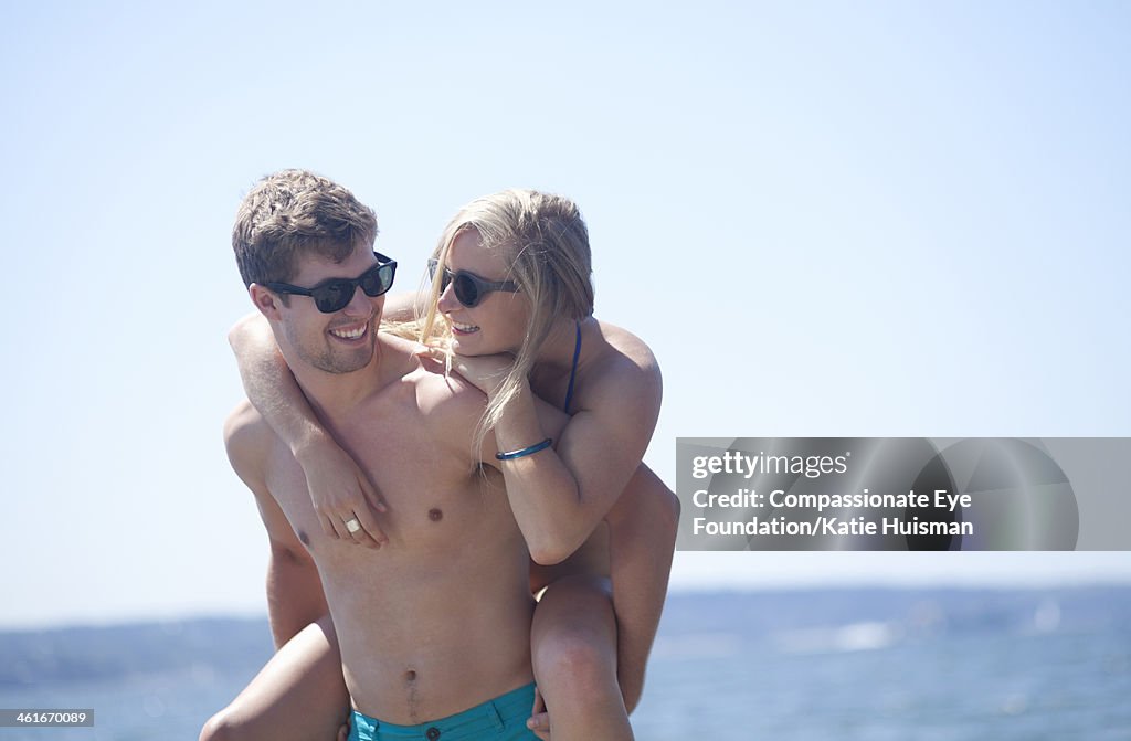 Man giving girlfriend piggy back ride on beach