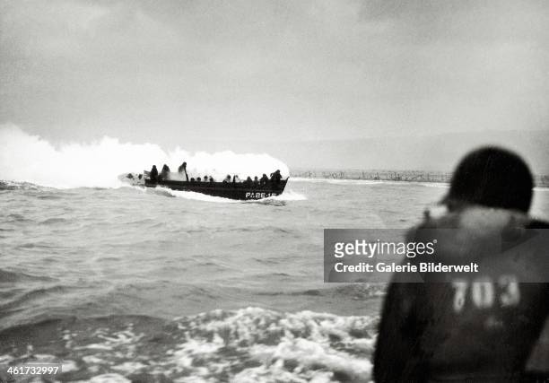 An U.S. Landing craft is approaching Omaha Beach. 6th June 1944. It is covered with thick white smoke. Barbed wire installations can be seen along...