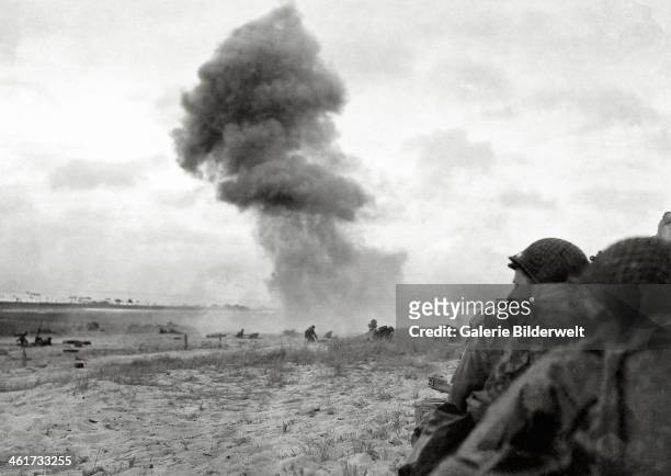 An 88 mm shell explodes on Utah Beach. 6th June 1944. In the foreground, U.S. Soldiers protect themselves from enemy fire. Normandy, France.
