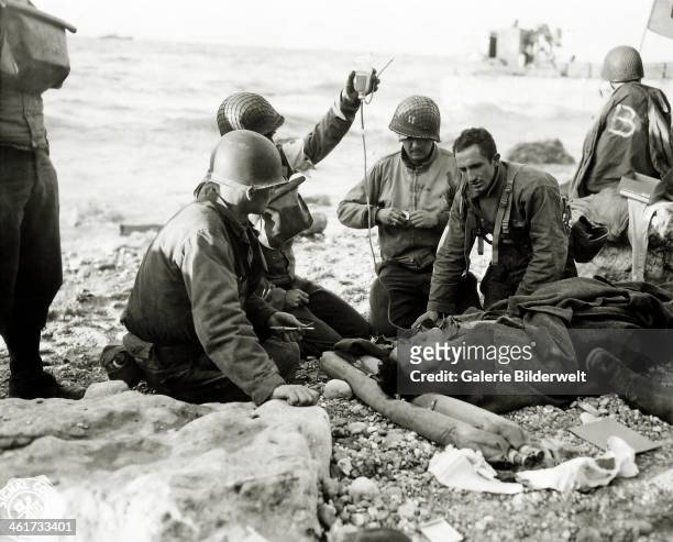 Nurses administer a plasma transfusion to a wounded survivor of a landing craft at "Fox Green" sector portion of Omaha Beach. 6th June 1944. The...