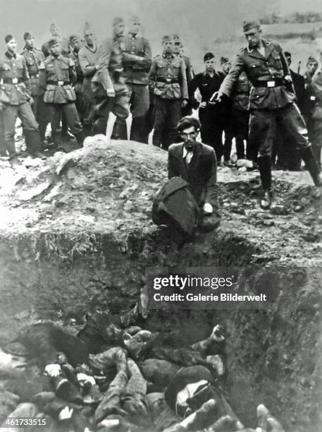 German soldier is about to shoot a Jewish man in Vinnytsia. 1941. The victim is sitting on the edge of an excavation with many dead bodies inside....