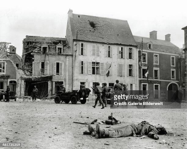 The body of a German soldier belonging to the 2. Infanterie Regiment is lying on the Market Square. 15th June 1944. The two jeeps in the center of...