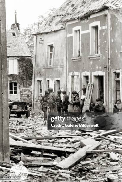 Soldiers are waiting in a street filled with rubble .16th June 1944. These are 2/505th PIR paratroopers of the U.S. 82nd Airborne with their...