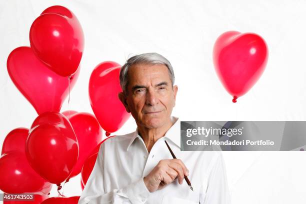 The Italian journalist Carlo Rossella poses thoughtful with a pen and some heart-shaped baloons . Pavia, 9th March 2012