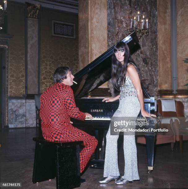 Faced backwards, the American singer Salvatore Philip Bono, known as Sonny, extemporizes a theme at the piano, while smoking a cigarette and looking...