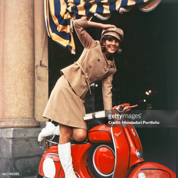 Cheerful portrait of Marisa Sannia who smiles while resting in balance on a red Piaggio Vespa; the Sardinian singer-songwriter wears a typical...