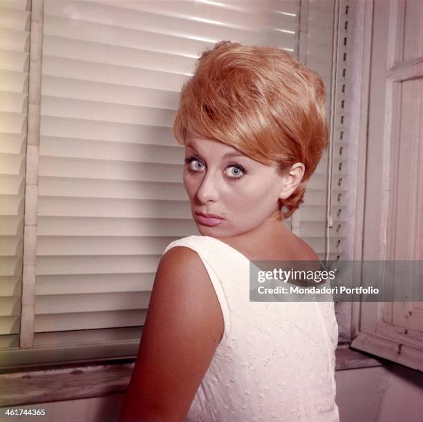 Sandra Mondaini, faced backwards towards the white shutter of a window, casts an amazed glance at the camera; the versatile Italian comic actress is...