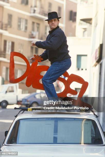 Italian stand-up comedian and actor Francesco Salvi on the hood of a car holding the writing diesel between his legs, referring to the catching...