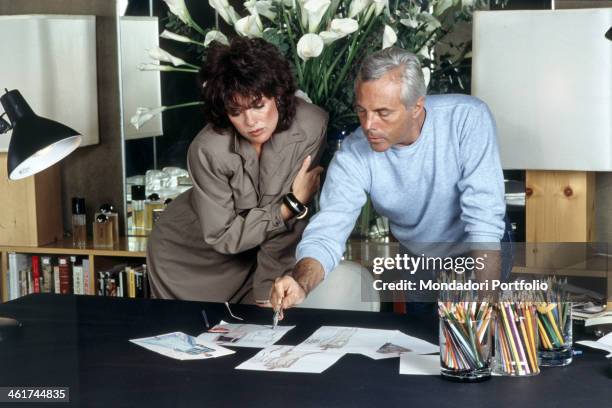 Italian fashion designer Giorgio Armani showing some sketches to American actress Linda Gray. 1983