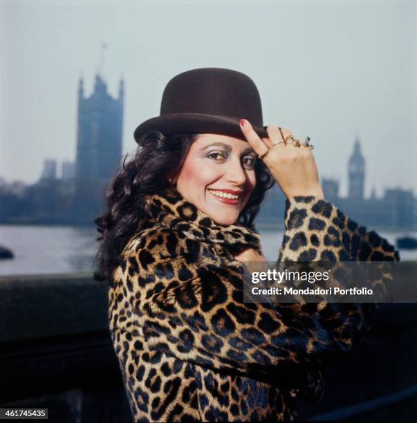 Italian singer Mia Martini posing smiling wearing a leopard-skin fur coat and a bowler hat. London, 1977