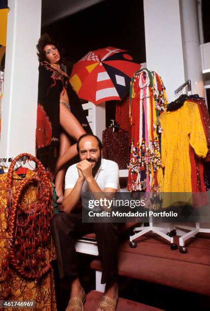 Italian fashion designer and entrepreneur Elio Fiorucci posing in his shop in Galleria Passarella. In the background, the shop assistant Cristina...