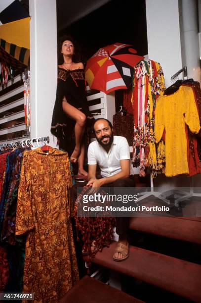 Italian fashion designer and entrepreneur Elio Fiorucci posing in his shop in Galleria Passarella. In the background, the shop assistant Cristina...