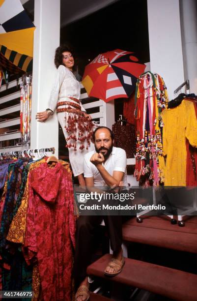 Italian fashion designer and entrepreneur Elio Fiorucci posing in his shop in Galleria Passarella. In the background, the shop assistant Cristina...