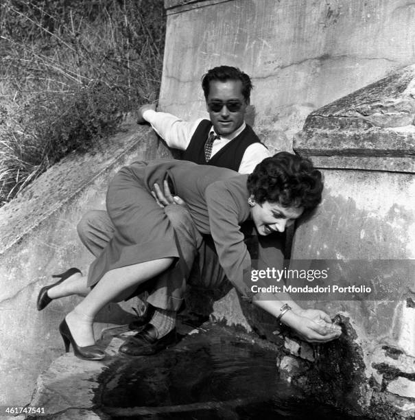 Italian actress Gina Lollobrigida drinking from a fountain held up by her husband, Slovenian doctor Milko Skofic. The actress and her husband are...