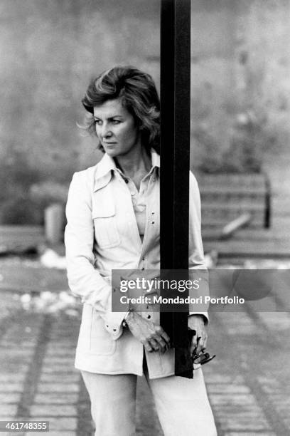 Well-dressed Marina Cicogna, wearing English-attitude white pants and jacket with belt of the same colour, looks far away, thoughtful, leaning...