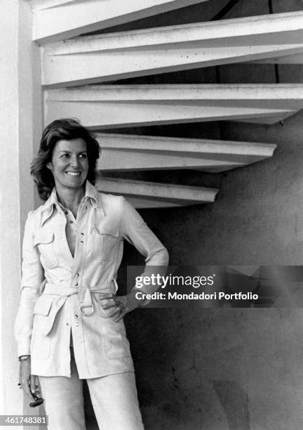 Knee-figure of the Italian actress and scriptwriter Marina Cicogna posing under a spiral staircase; representative of the Sixties jet set, she...