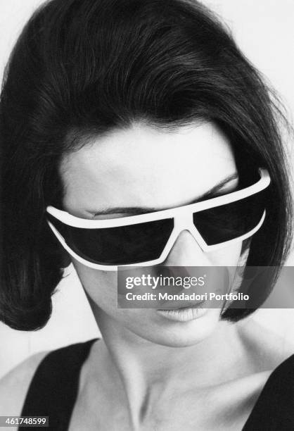 Close-up of a model who shows off big black flashy sunglasses with a thick white frame, advertising a new line with an aggressive design for women in...
