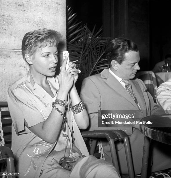 Isa Barzizza looks into the lens of a Minox AIII, ready to take a photograph; the famous revue actress is seated at the outdoor table of a bar beside...