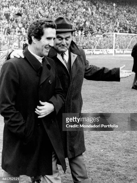 Italian coach Nereo Rocco walking on a football ground with Argentinian-born French coach Helenio Herrera. 1972
