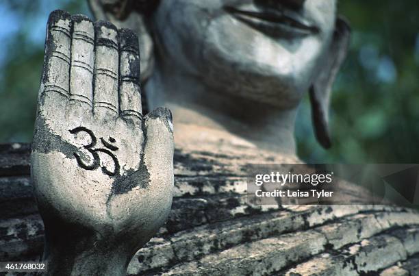 Standing Buddha holds up a hand inscribed with the mantra Om. Originally a Hindu symbol, the mantra is also sometimes seen associated to Mahayana or...