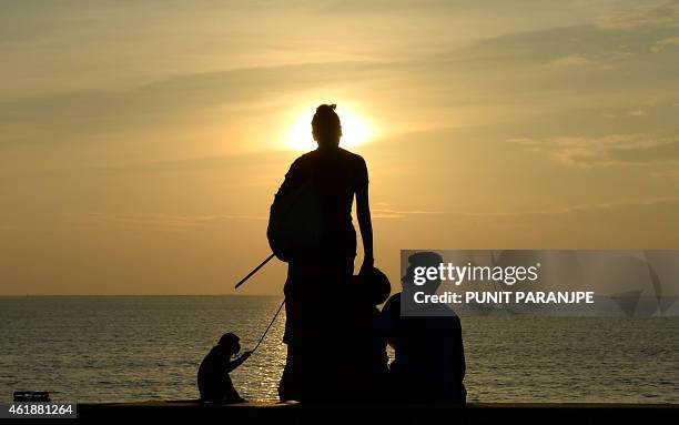 An Indian woman keeps her pet monkey on a leash as she asks for alms from a couple sitting at the seafront in Mumbai on January 21, 2015. India is...