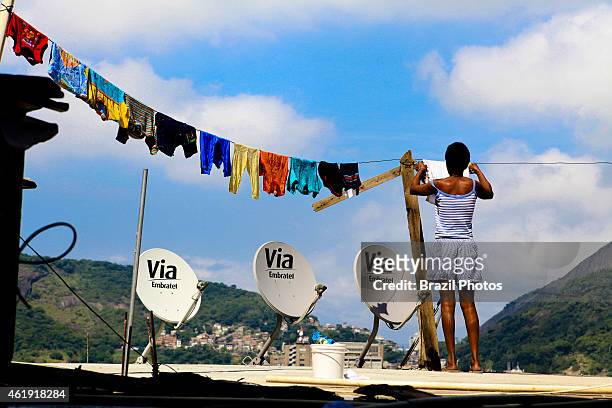 Woman hanging clothes on her house slab-cover at top of Favela Santa Marta sharing space with domestic satellite television receiving dishes that are...
