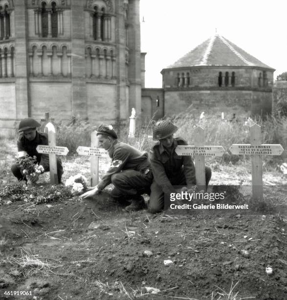 Three soldiers of the 23rd Field Ambulance of the 3rd Canadian Infantry Division place flowers on graves. June 1944. Two soldiers wear the armband...