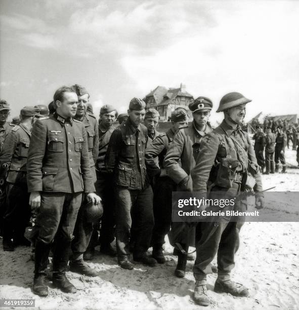 Canadian soldier stands at the head of a group of German prisoners of war, including two officers, on Juno Beach at Bernières-sur-Mer, Normandy,...