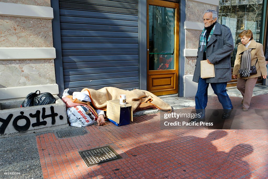 Greeks walk by a homeless man sleeping on the pavement in...