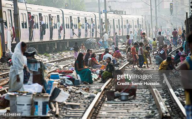 People get on with their lives in a slum on the railway tracks as a commuter train goes past on December 12, 2013 in Kolkata, India. Almost one third...