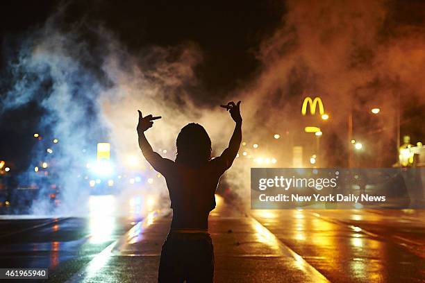 Protester gestures angrily at cops as tear gas fills the streets of Ferguson after curfew early Sunday. One person was gravely injured in shooting,...