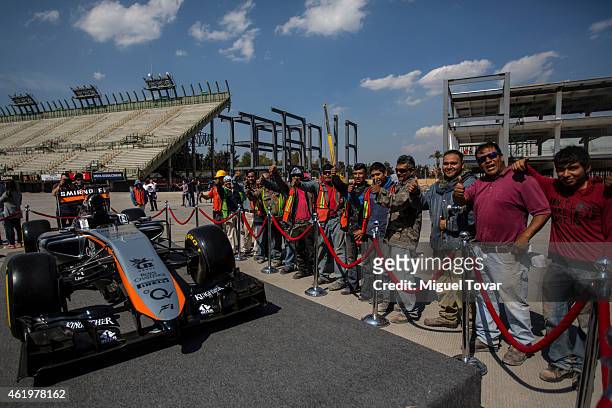 Workers pose for pictures next to the F1Team Force's India new car at the Hermanos Rodriguez Racing Circuit Facilities on January 22, 2015 in Mexico...