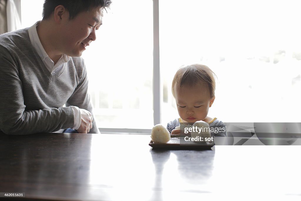 Father with son eating rice ball at table