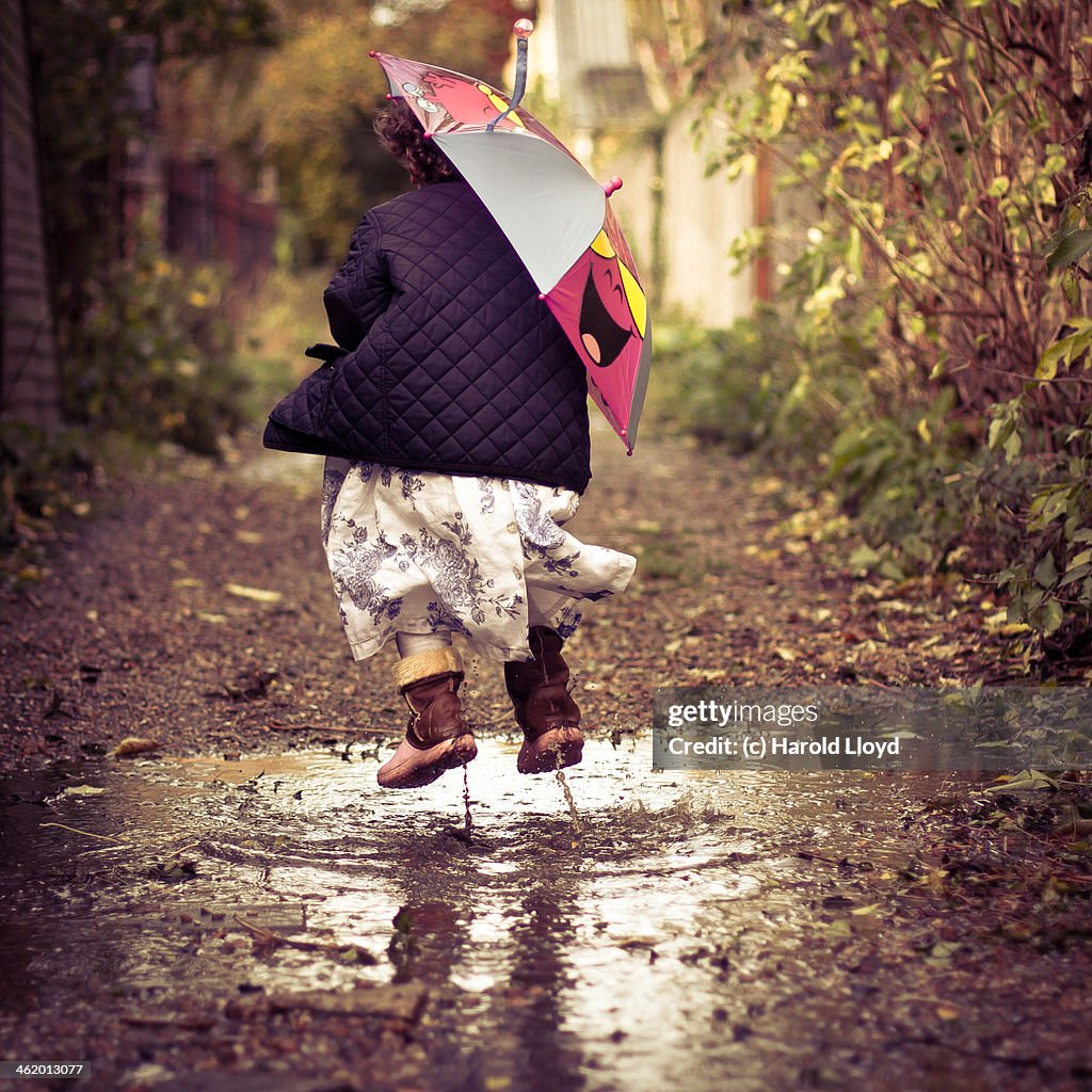 Girl muddy puddle jumping with smiling umbrella