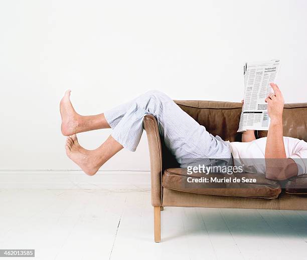 man laying on sofa with newspaper - casual man white background stock-fotos und bilder