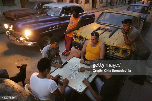 Men hold a board up with their knees while playing a game of dominoes in Centro Habana, the most densely populated neighborhood in the city, January...